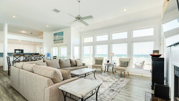 A spacious living area with a large sectional sofa, a coffee table, and a fireplace. There are multiple windows providing a view of the ocean. - Beachfront w/ Huge Deck, Dog Friendly, Dune Walkover, Feel Right at Home! (Galveston)
