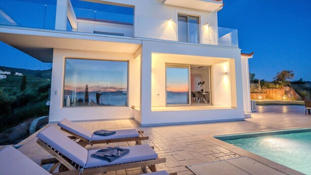 En modern villa med en swimmingpool, stora fönster och en terrass med solstolar.