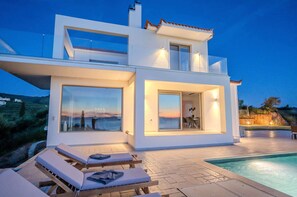 A modern villa with a swimming pool, large windows, and a terrace with lounge chairs. - Villa Sadova Summary: (Kalamata)