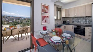 A modern kitchen with a view of the city, a dining area with a glass table, and a balcony with a table set for two.