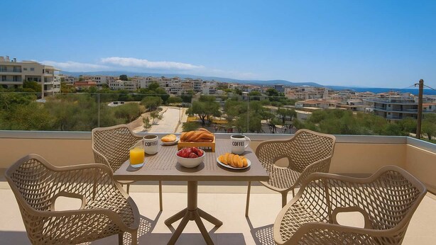 A balcony with wicker chairs, a table with breakfast items, and a view of a coastal town.