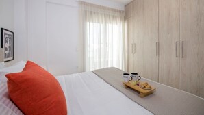 Ett hotellrum med en säng, en garderob i trä, ett fönster med gardiner och ett bricka med muggar och bakverk.
