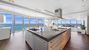 Une cuisine moderne dotée d’un grand îlot central, d’appareils électroménagers en acier inoxydable et offrant une vue sur l’océan.