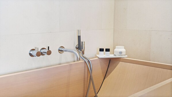 Un baño moderno con una bañera de madera, un cabezal de ducha manual y un estante con artículos de aseo.