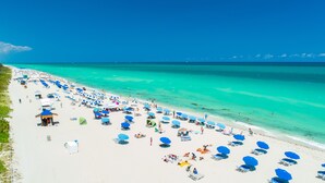 Une plage parsemée de nombreux parasols bleus et de chaises longues blanches.