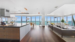 Un intérieur moderne comprenant une cuisine, un coin repas et un salon, avec de grandes fenêtres et une vue sur l’océan.