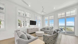 A spacious living room with a large window, a flat-screen TV, and a ceiling fan.