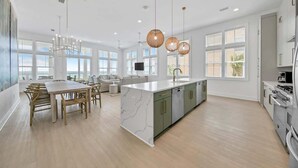 A spacious kitchen with a marble island, wooden dining table, and pendant lighting.
