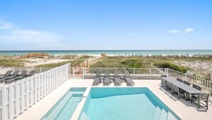 A rooftop pool with lounge chairs and a table, overlooking a beach with a clear sky.