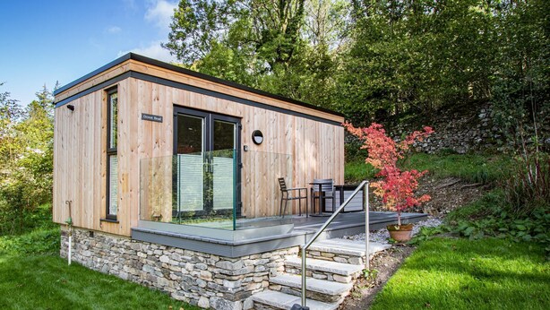 Een moderne houten chalet met een stenen fundering, een glazen deur en een klein zitgedeelte buiten.