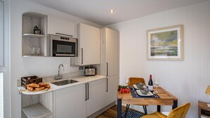Een compact keuken voorzien van een magnetron, broodrooster en een klein spoelbakje. Er staat een eettafel gedekt met een fles wijn, glazen en een schaal.