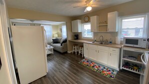 A compact kitchen with white cabinets, a refrigerator, a microwave, and a window with blinds. - Cozy cottage for a couple's weekend get away! (Russells Point)