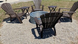 A set of Adirondack chairs arranged around a circular metal table on a gravel surface. - Cozy cottage for a couple's weekend get away! (Russells Point)