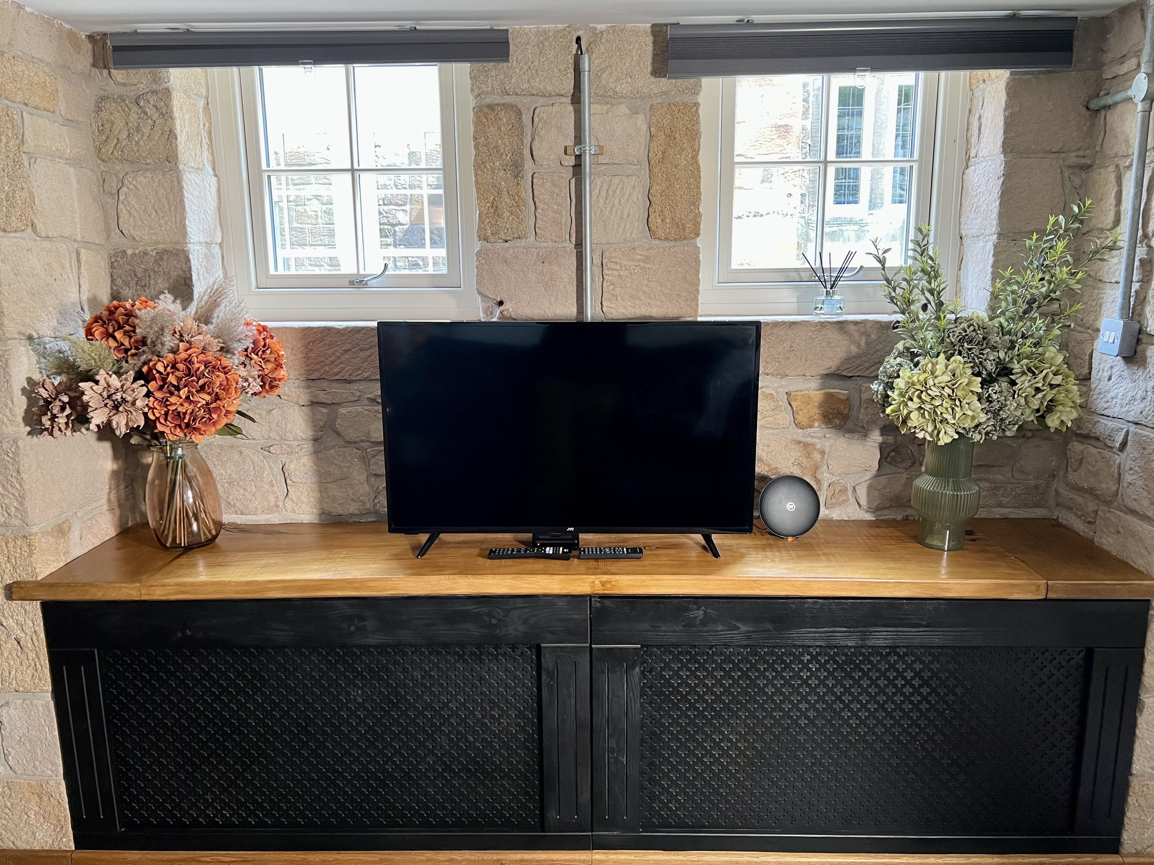 A TV on a wooden stand with stone walls and windows.