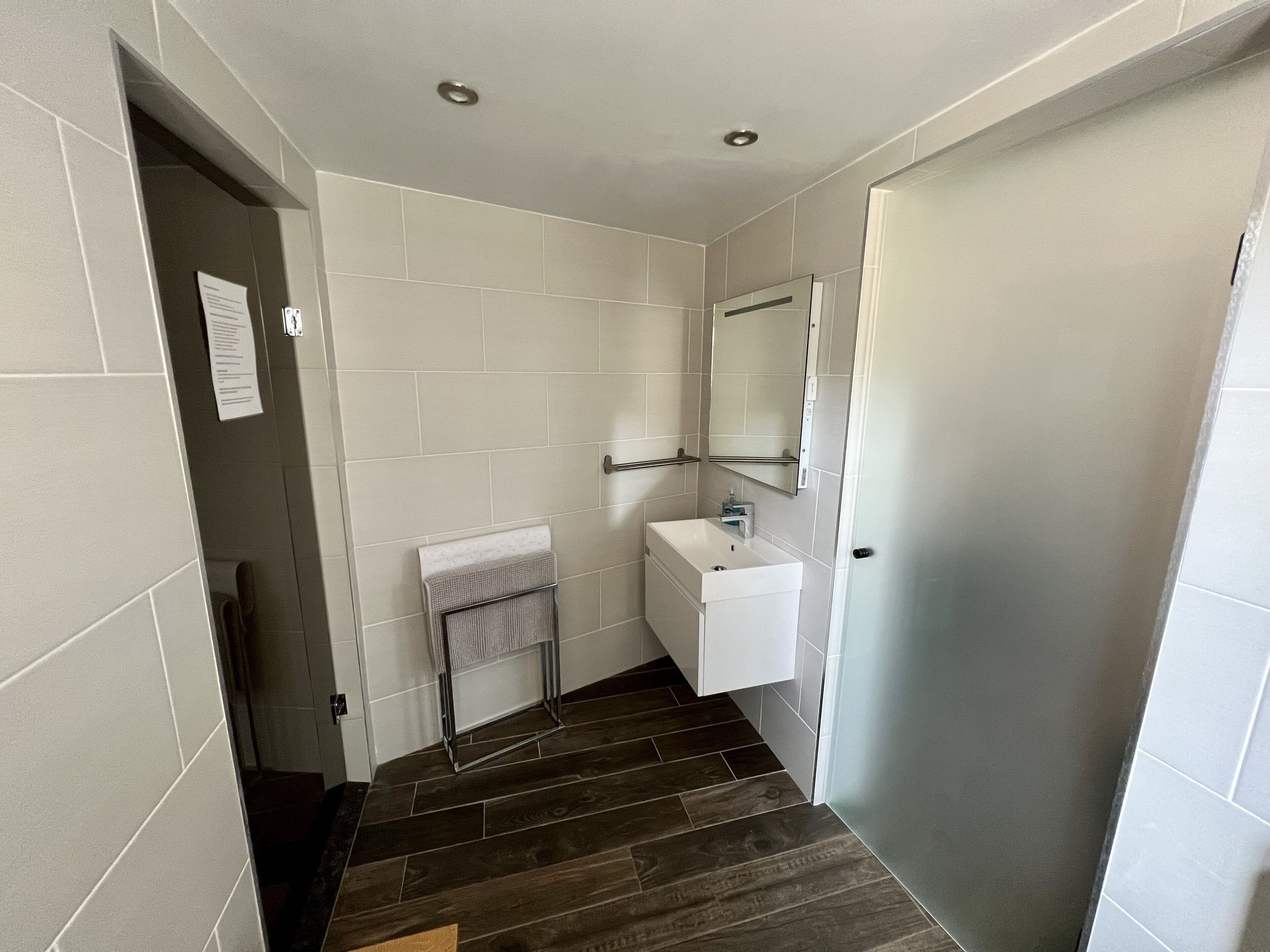 Un bagno con piastrelle bianche, un lavandino bianco, uno specchio e un portascopino.
