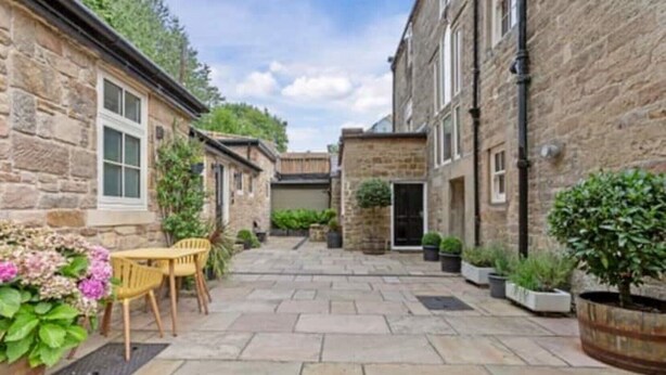 A stone courtyard with a table and chairs, surrounded by potted plants and a stone wall. - Luxurious Bolthole (Matlock)