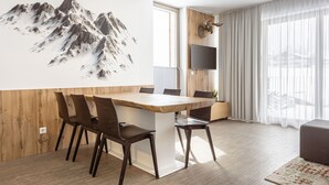 A modern dining area with a wooden table and chairs, a mounted TV, and a mountain artwork on the wall.