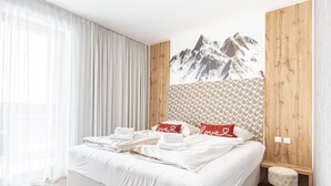 A neatly made bed with white linens and two pillows with 'love' written on them, a wooden headboard, and a mountain landscape mural on the wall.