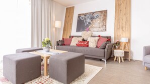 A modern living room with a grey sofa, two grey ottomans, a wooden coffee table, and a floral rug.