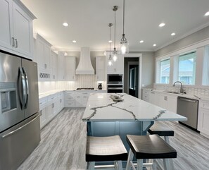 A modern kitchen with white cabinetry, a marble island, stainless steel appliances, and pendant lighting. - 5TH ROW - DRIFTWOOD - 4 BEDROOM - 3 BATH - SLEEPS 17 (Crystal Beach)