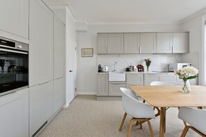 Une cuisine moderne avec des meubles blancs, une table à manger en bois et un vase de fleurs.