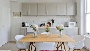 Une cuisine moderne avec des armoires blanches, une table en bois et des chaises blanches. On peut voir des vases remplis de fleurs sur la table.