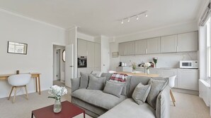 Un salon moderne avec un canapé gris, une table basse rouge et une cuisine en arrière-plan.