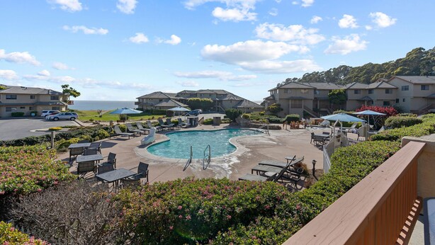 A pool area with lounge chairs and umbrellas, surrounded by buildings with a view of the ocean. - Closely located to Seascape Golf Course & Seascape Village (Aptos)