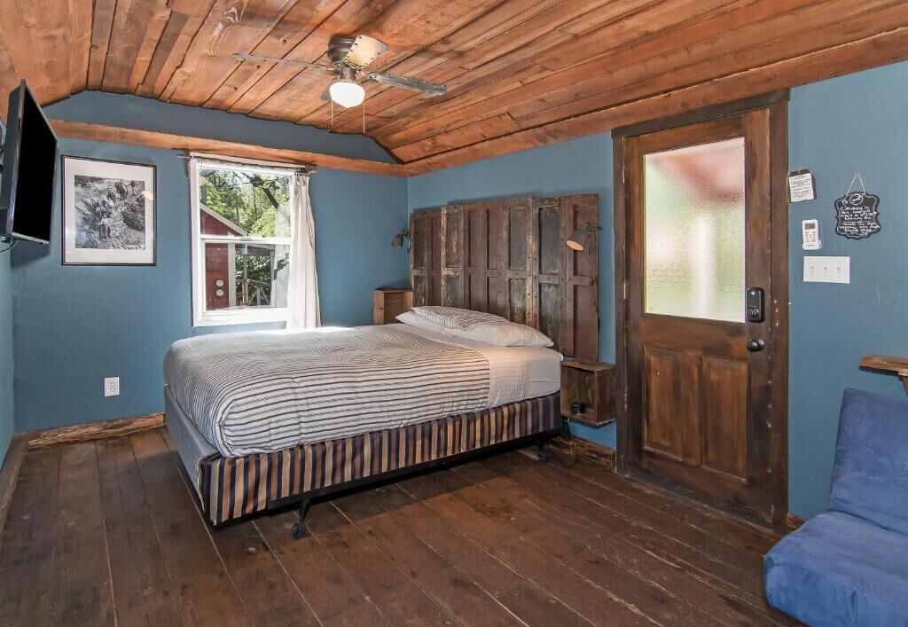 Un dormitorio con techo de madera, una cama con ropa de cama a rayas, una ventana y una puerta con panel de vidrio satinado.