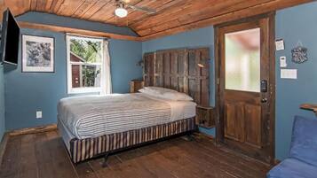 Un dormitorio con techo de madera, una cama con ropa de cama a rayas, una ventana y una puerta con panel de vidrio satinado.