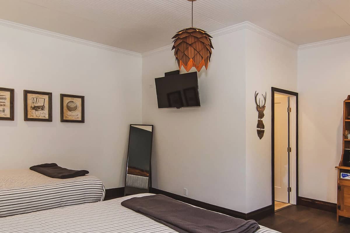 A hotel room with two beds, a large mirror, a wooden door, and a ceiling light fixture.