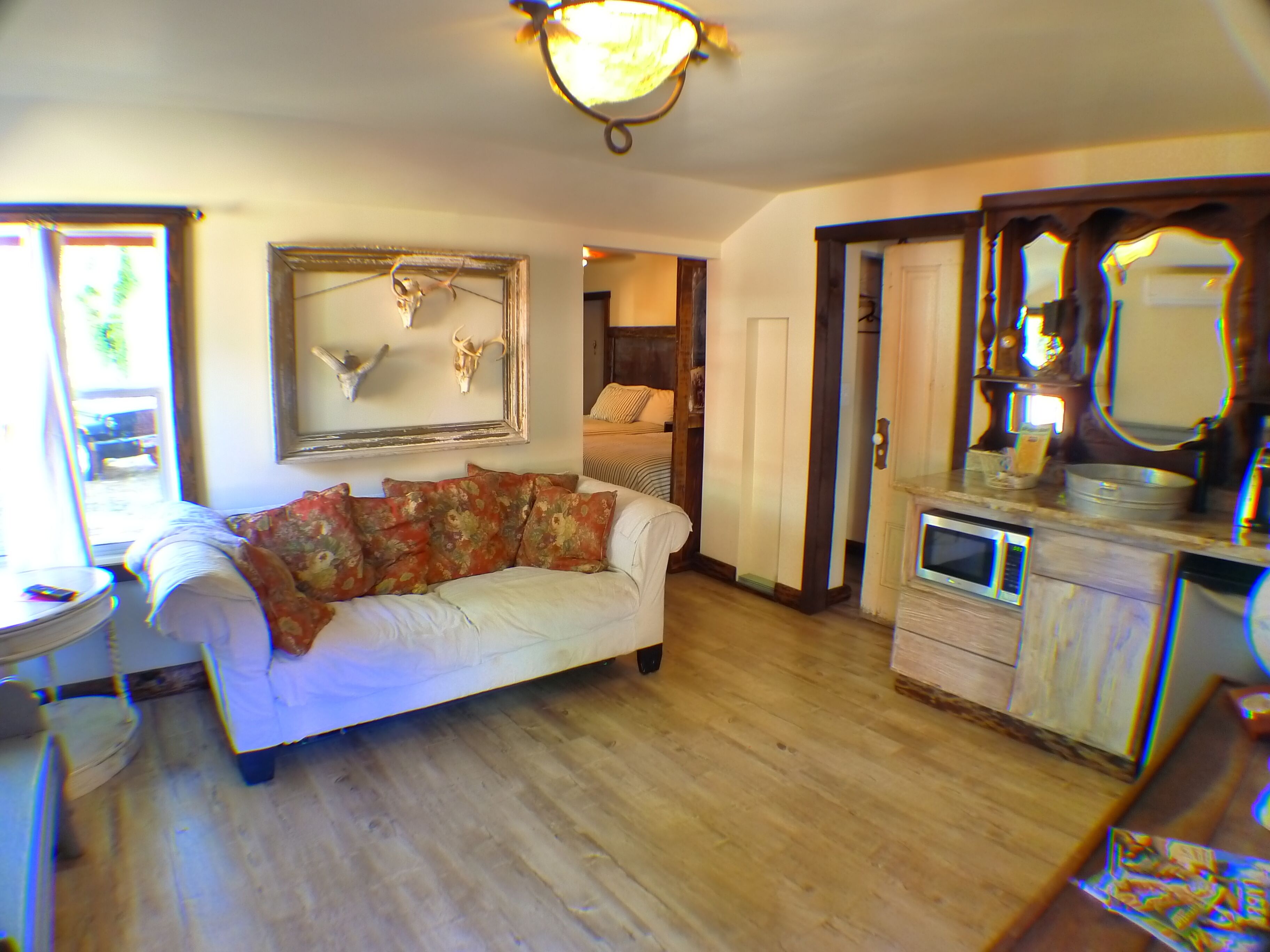 A cozy living room with a white sofa, a wooden floor, a dining area with a microwave, and a hallway leading to another room.