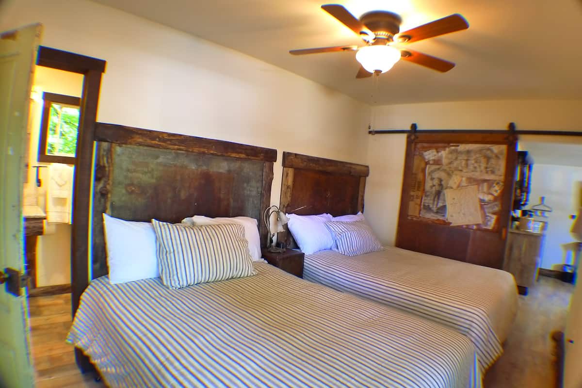 A room with two beds, wooden headboards, a ceiling fan, and a door with a bulletin board.