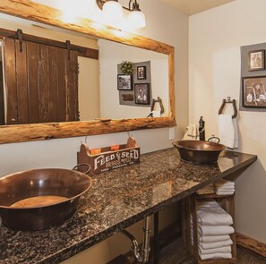A bathroom with a granite countertop, two sinks, a wooden-framed mirror, and a towel rack. - Miners Camp (Foresthill)