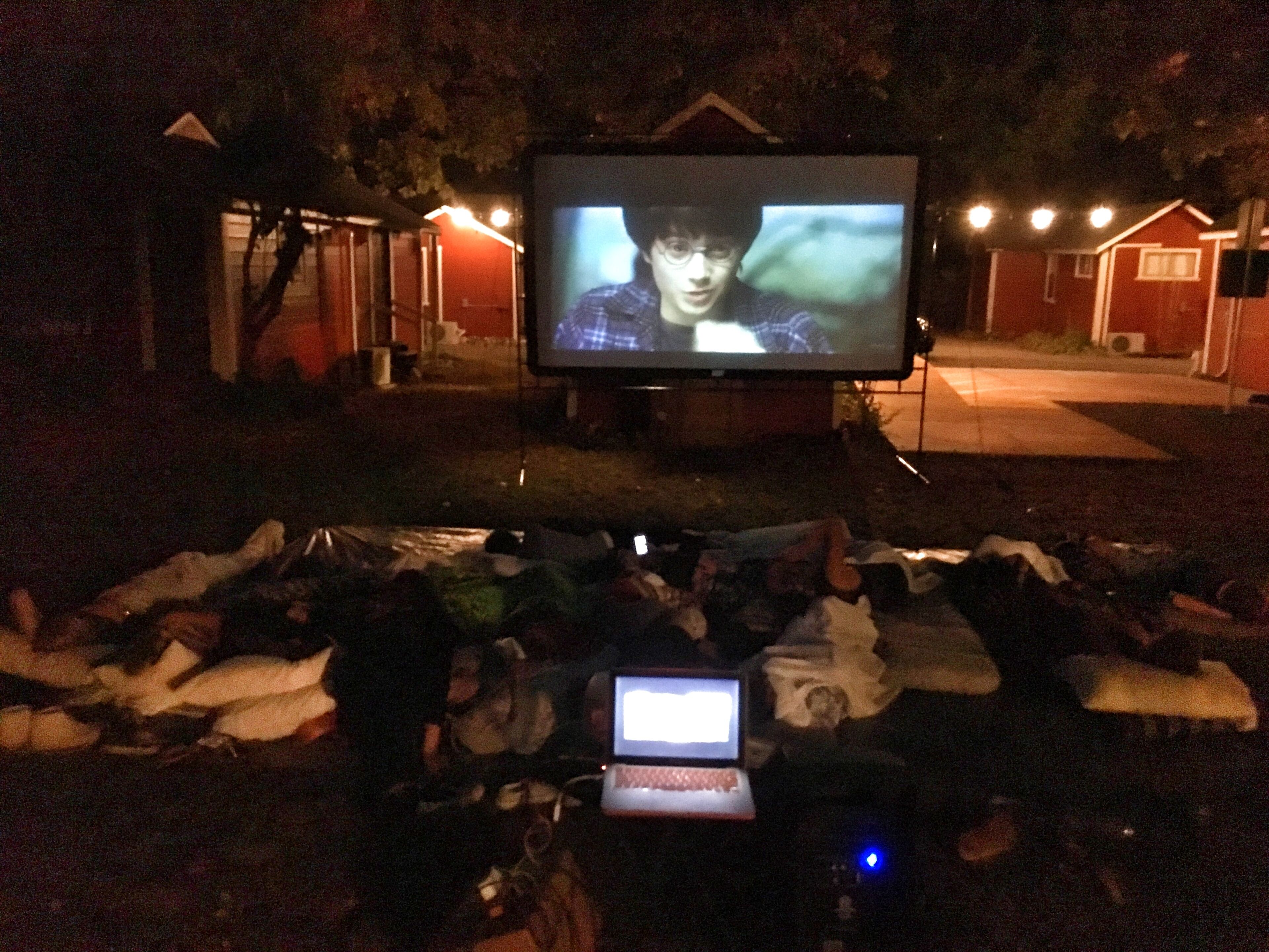A television and laptop on a table outdoors at night.