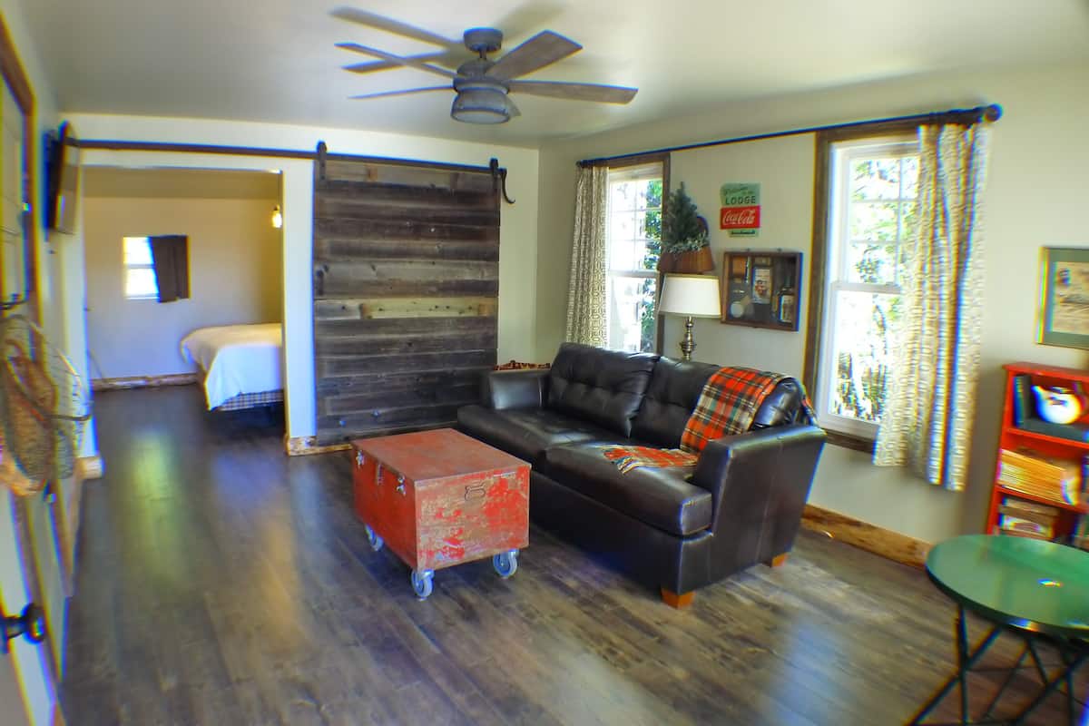 A living room with a black leather sofa, a red storage box, a ceiling fan, and a window with curtains.