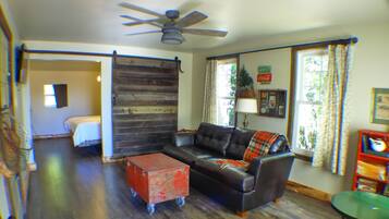 A living room with a black leather sofa, a red storage box, a ceiling fan, and a window with curtains.