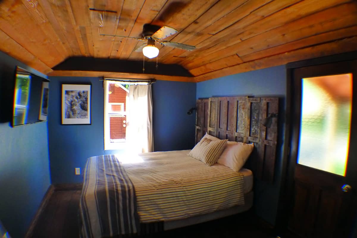 A bedroom with a wooden ceiling, a bed with striped bedding, and a door with a view of the outside.