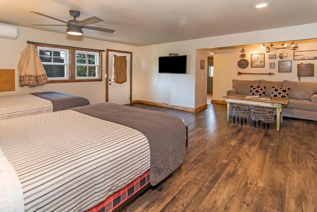 A room with two beds, a ceiling fan, a television, a couch, and a coffee table.