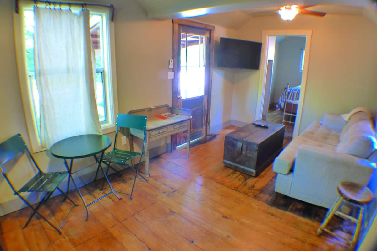 A living room with a sofa, a small table, a chair, and a TV mounted on the wall.