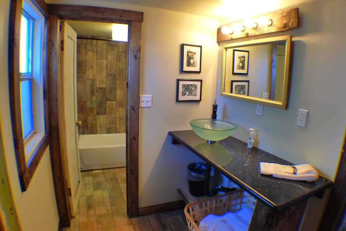 A bathroom with a glass sink, a mirror, and framed pictures on the wall.