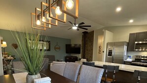 Une cuisine moderne équipée d’appareils électroménagers en acier inoxydable, un coin repas avec une table et des chaises en bois, et un ventilateur de plafond.