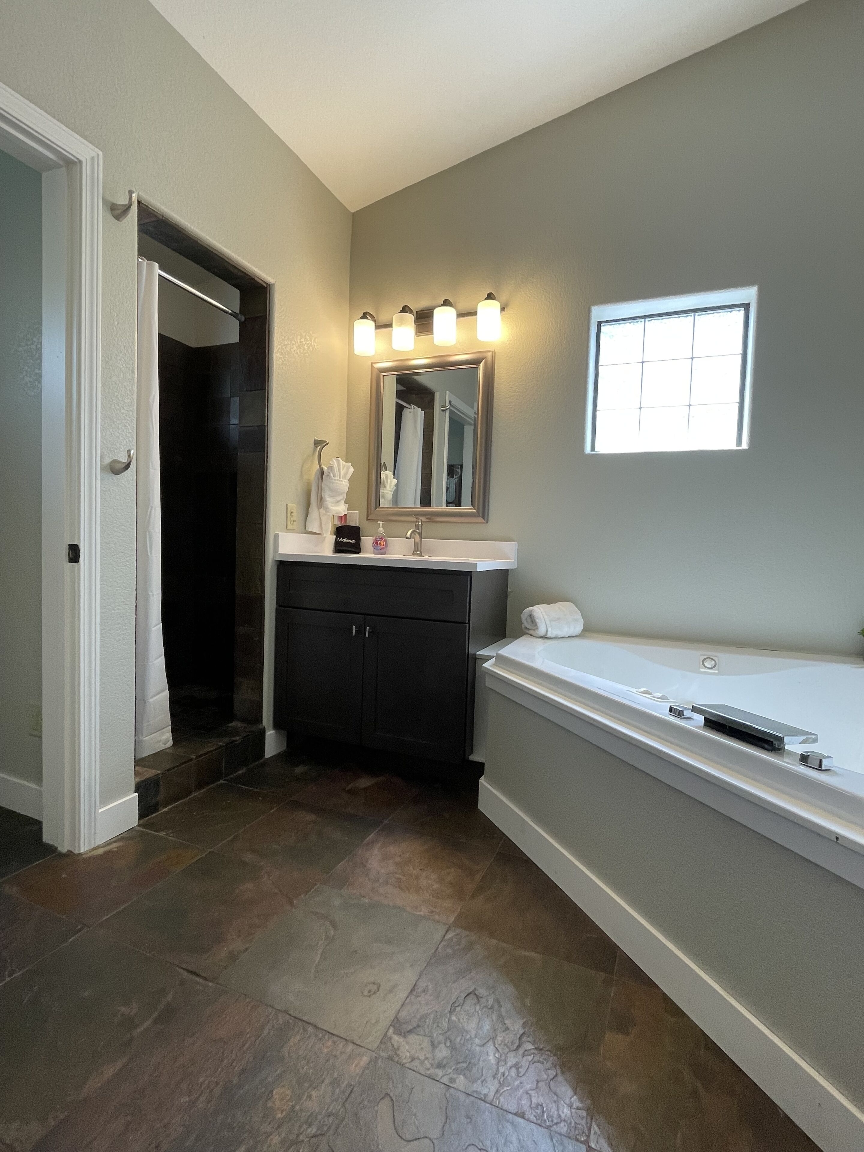 A bathroom with a dark tiled floor, a white sink with a mirror above it, and a window with natural light.