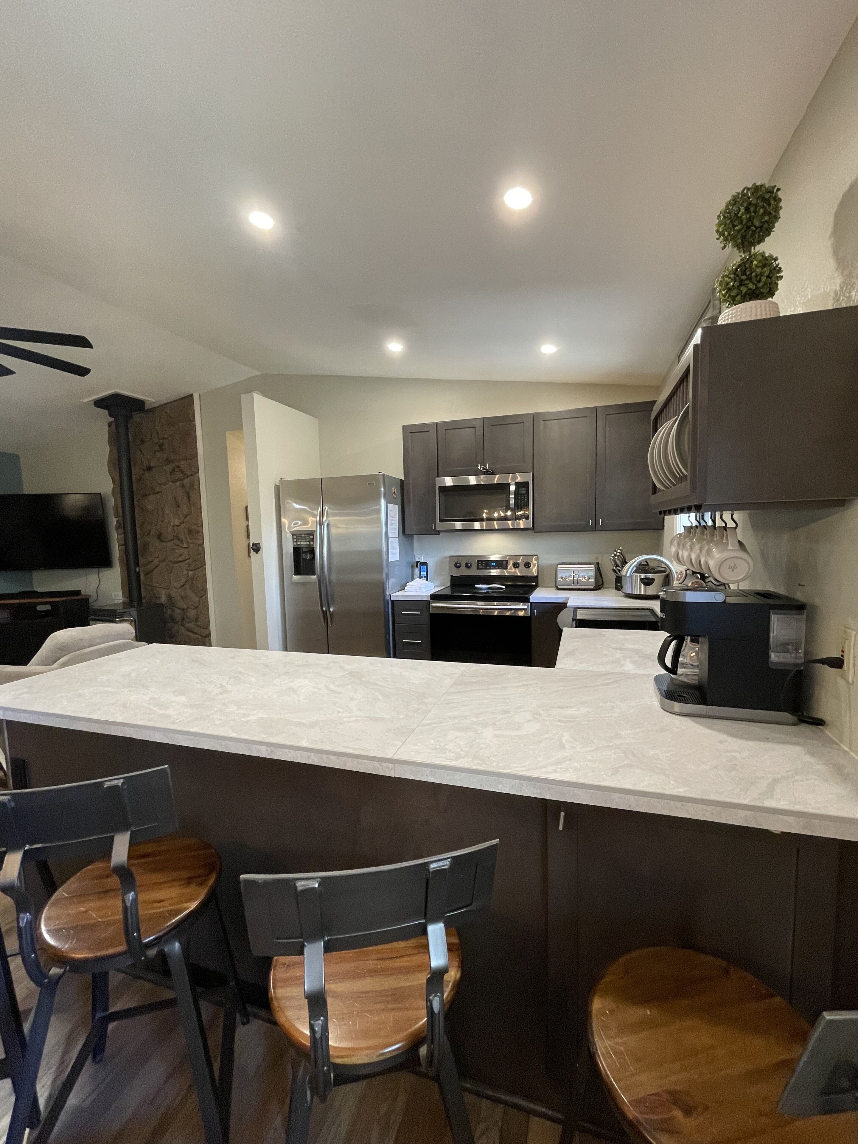 A modern kitchen with a central island, bar stools, a built-in oven, microwave, and a coffee machine.