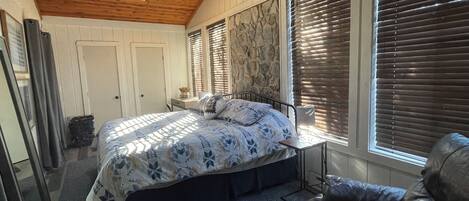 Un dormitorio con cama, ventilador de techo, ventana con persianas y techo de madera.