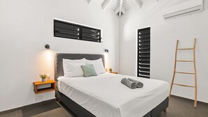 A modern bedroom with a large bed, a wooden ladder, and a small bedside table with a plant.