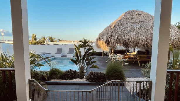 A pool area with a thatched-roof structure, lounge chairs, and tropical plants.