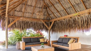 A covered outdoor seating area with wooden furniture and a thatched roof.