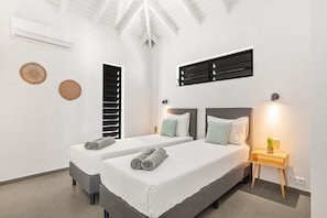 A modern hotel room with two beds, a ceiling fan, a wall-mounted air conditioner, and a bedside table with a lamp.