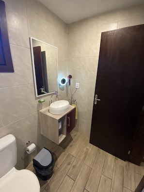 Un baño con inodoro, lavamanos, espejo y un armario de madera.